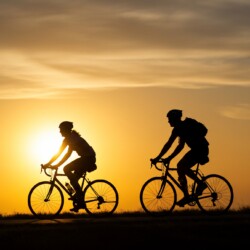 Two silhouetted cyclists ride their bikes along a path as the sun sets, creating a golden and dreamy atmosphere. This serene image could be used for travel, fitness, or inspirational content.
